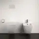 Weißes WC und Bidet von Ideal Standard an einer hellen Wand, neben einem Wandpapierhalter. Minimalistische Gestaltung ohne sichtbare Spülarmaturen.